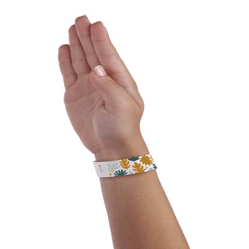 wrist wearing a white tyvek wristband with silver, gold and green leaves pattern