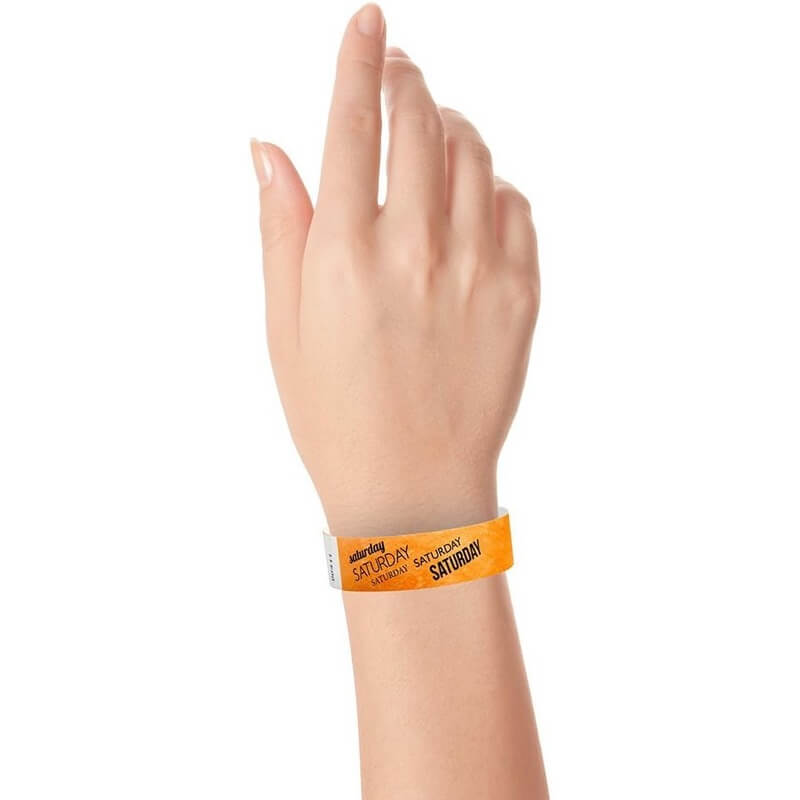 hand wearing neon orange tyvek wristband with saturday text in black ink repeated