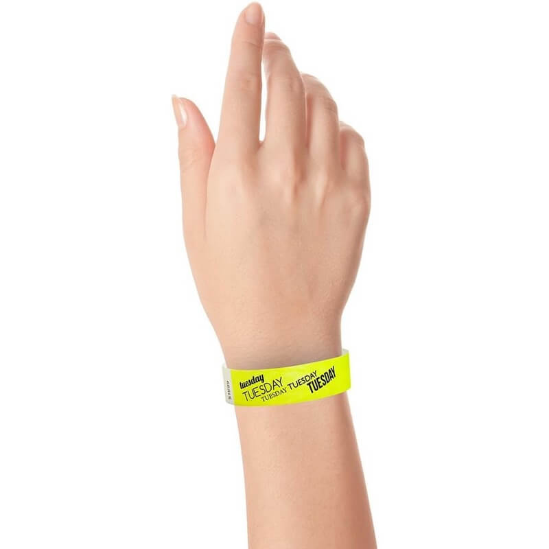 hand wearing neon yellow tyvek wristband with tuesday text in black ink repeated