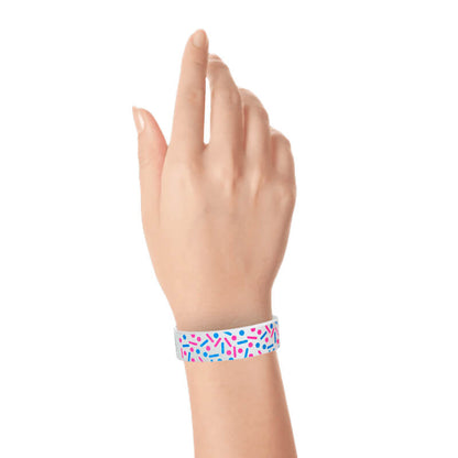 Hand wearing a colourful sprinkle pattern in neon pink and neon blue on a white tyvek wristband